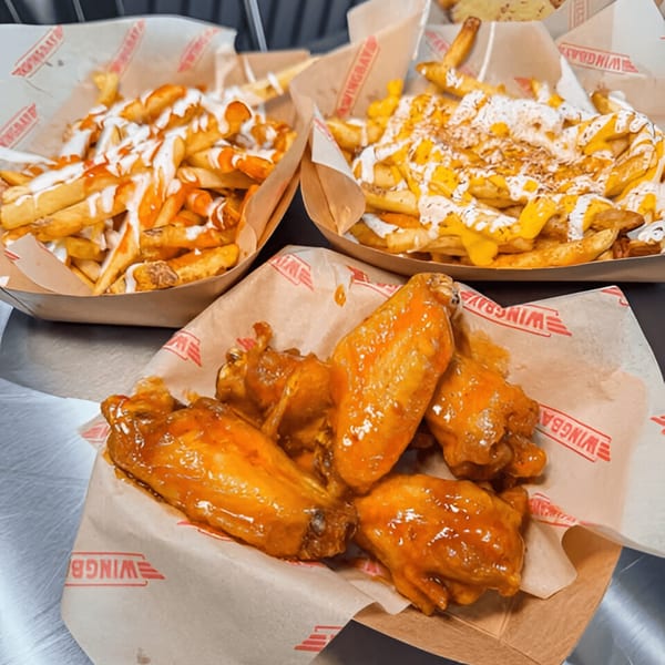 Wingbay's glazed chicken wings and two trays of loaded fries with various toppings.