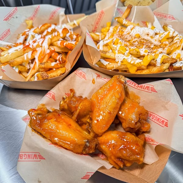 Wingbay's glazed chicken wings and two trays of loaded fries with various toppings.