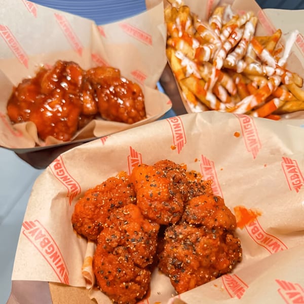 Wingbay's boneless wings in two flavors and fries with sauce, served in branded paper-lined baskets.