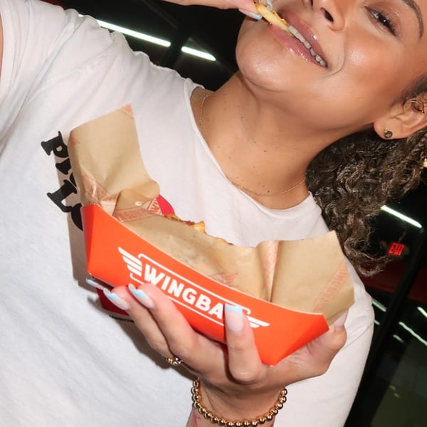 A woman in a white shirt eating fries from a red Wingbar container.
