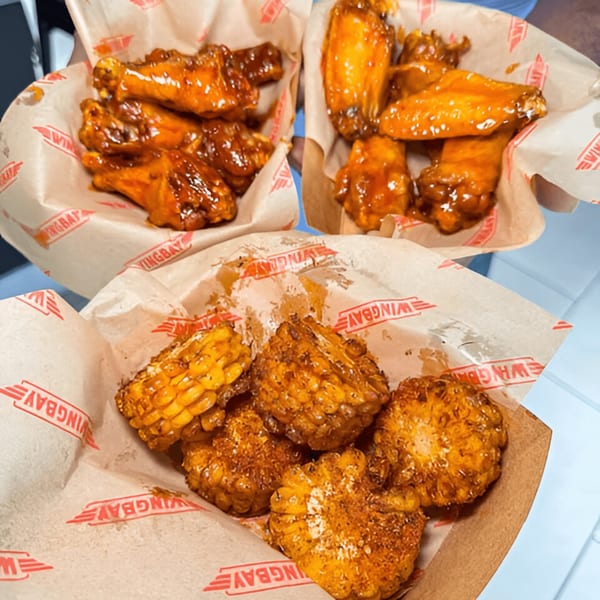 Three Wingbay baskets, two with glazed chicken wings and one with seasoned corn on the cob.